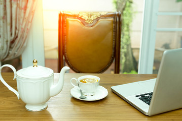 Tea with slice of lemon in white cup with teapot and notebook at