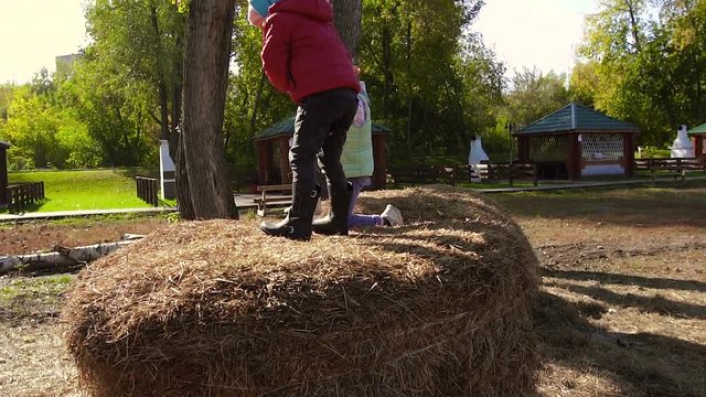 Little friendly girl helping another girl climb onto haystack and then jumping down