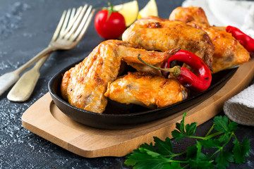 Grilled chicken wings on a cast iron pan on a black oval stone background. Selective focus.