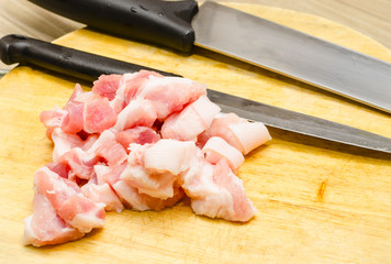 raw pork cutted to small piecs on cutting board with kitchen knife