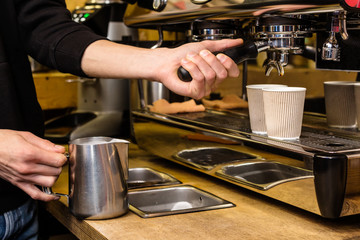 Barista preparing to add milk for takeaway coffee.