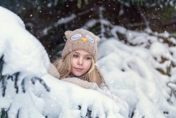 Fototapeta na wymiar Attractive young blonde girl walking in winter forest. Pretty woman in wintertime outdoor. Wearing winter clothes. Knitted sweater, scarf, hat and mittens.