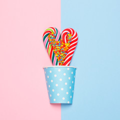 Top view of a colorful candy cane in a heart shape on a pastel blue and pink background. Minimal concept