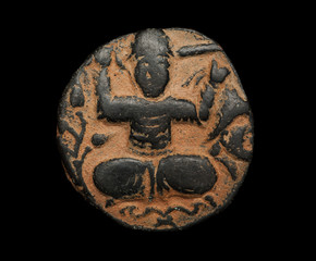 Ancient bronze coin with image of person seated in lotus position isolated on black