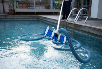 Man cleaning swimming pool with vacuum tube cleaner
