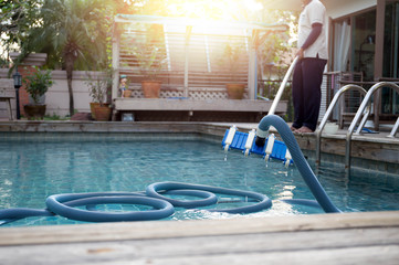 Man cleaning swimming pool with vacuum tube cleaner
