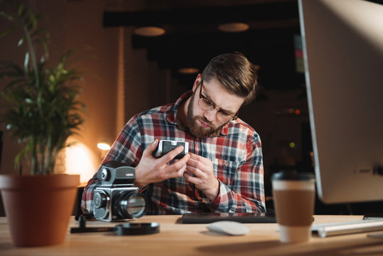 Young bearded man in shirt trying to fix old camera