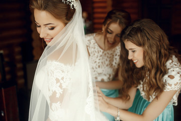 Beautiful bridesmaids adjust bride's dress standing in the room