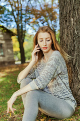 Beautiful girl with long blond hair and blue eyes talking on the phone. Location of autumn park.