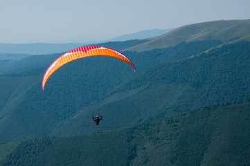 Paragliding in the Carpathians mountains. Pilot flying in the sky under mountains.