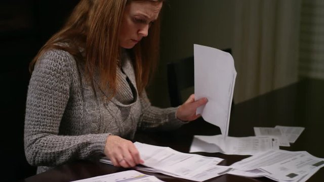 A woman looking over bills at the table, looking stressed