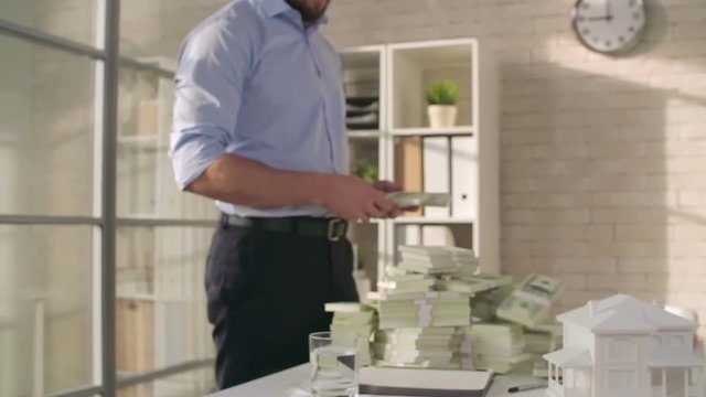 Zoom in of businessman standing in the office and throwing money stacks on table