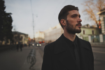 Lone stylish young man with a beard in a black coat on the street