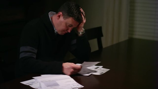 A man looking over bills at the table and looking stressed, and throws papers