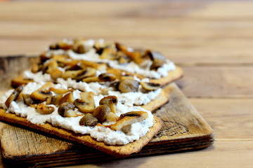Healthy open sandwiches on a wooden board. Sandwiches with soft cheese and mushrooms on crisp bread. Tasty vegetarian snack. Closeup 