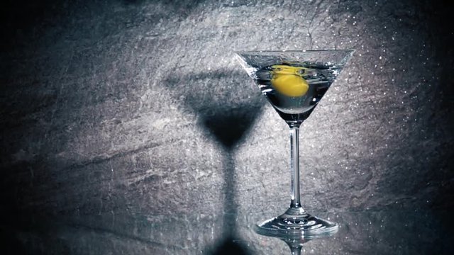 Olives falling in cocktail glass in slow motion. Close up film clip of coctail served in bar.