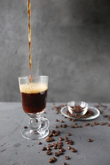 hot coffee in the tall glass with coffee beans on the grey stone table.