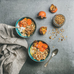 Healthy vegetarian breakfast. Oatmeal, quinoa granola with yogurt, dried fruit, seeds, honey, persimmon in bowls over grey background, top view, square crop. Gluten free, allergy-friendly concept