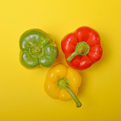 Three colorful paprikas on yellow background - Minimal flat lay