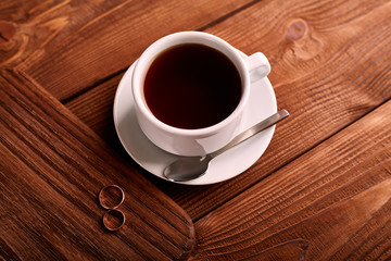 Black, flavored, organic coffee in white classic cup on a wooden table with a pair of wedding rings.