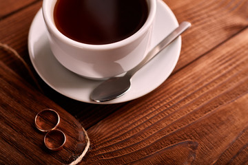 Black, flavored, organic coffee in white classic cup on a wooden table with a pair of wedding rings.