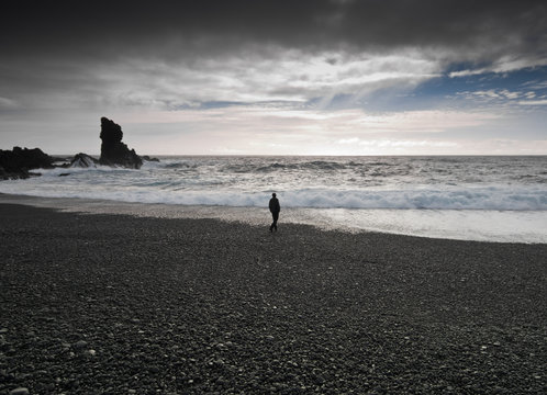 Man walking along black beach, djupalonssandur, snaefellsnes, iceland