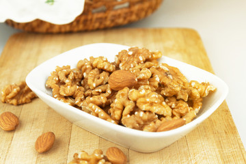 Wallnuts and almonds in earthenware pot on wooden chopping board with basket in frame