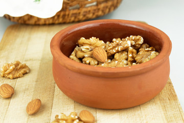 Wallnuts and almonds in earthenware pot on wooden chopping board with basket in frame