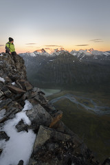 Fulfilled male hiker sitting on edge of a cliff enjoying the sunset colored landscape 