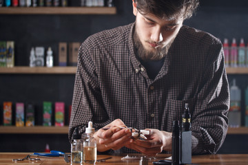 Vape. One man in a vape bar (shop) is repairing e-cigarette.