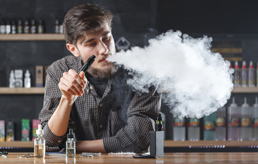 Vape bar (shop). Vaping man is smoking e-cigarette. A cloud of vapor.