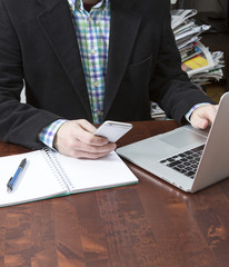 Business man working. The man is using a mobile phone. Laptop and a notepad next to him on a wooden table. Business concept image.