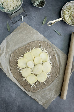 Pie dough and ingredients for a potato galette. Photographed on a greay background from top view.