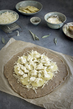 Pie dough and ingredients for a potato galette. Photographed on a greay background from top view.