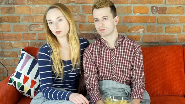 Absorbed couple sitting on the sofa under blanet and watching tv, steadycam shot
