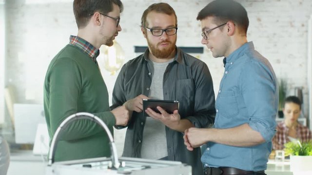 Three Creative Men Discuss Business Matters Passing Tablet Computer to Each Other. People Work in Background. Shot on RED EPIC (uhd). 