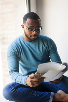 Young man reading a booklet sitting by the window