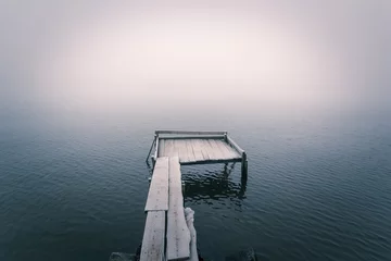 Stickers muraux Jetée Frozen wooden pier on a cold foggy river and smooth reflection on water. .