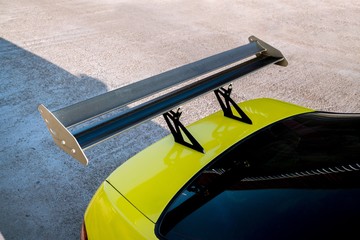 car part ; Close up detail of a custom racing carbon fiber spoiler on the rear of a yellow car