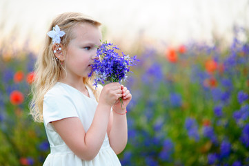 Beautiful little child wearing white dress smelling wild blue 