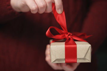 female teen hands opens craft paper gift box with red bow