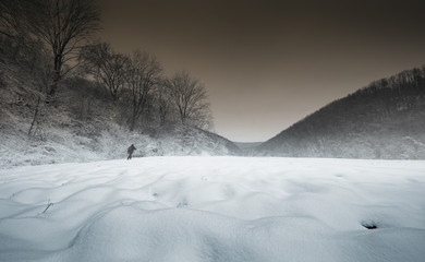 Man hiking in winter. Landscape with snow on the ground, dark sky, trees and man silhouette