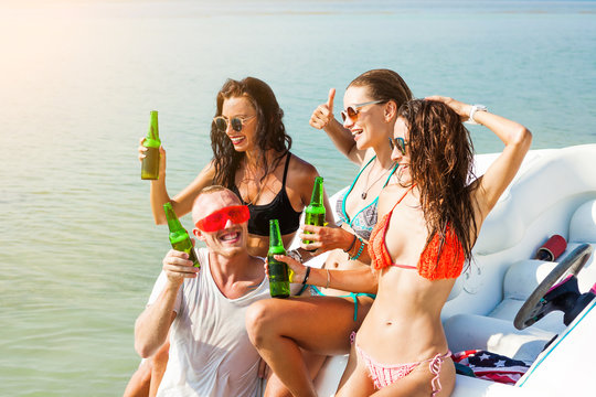 Three beautiful girls and a guy in funny glasses drinking beer near the speed boat, on the beach, sexy bikini, fashion accessories, merry company, happy, crazy emotions, pretending grimaces, laughs