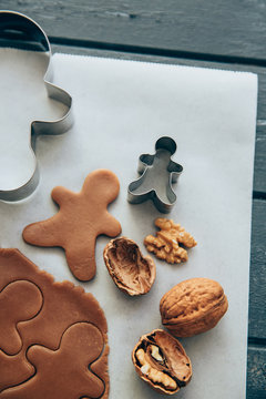 Close-up overhead view of Gingerbread men cookie dough, a cookie cuter and walnuts on a chopping board