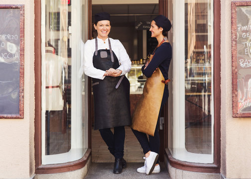Two women in aprons leaning in entrance to cafe