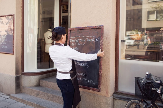 Rear view of female owner putting blackboard on wall outside grocery store