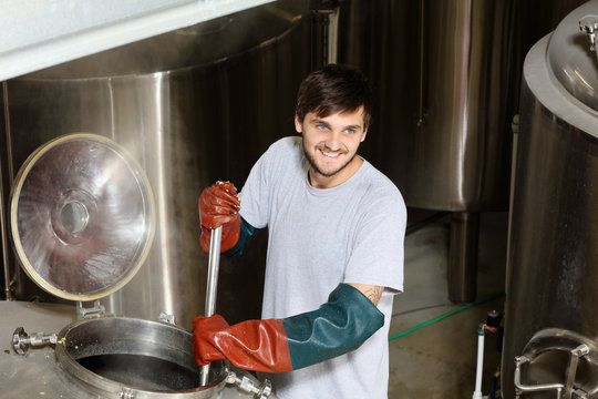 Worker in brewery, adding hops to brew kettle