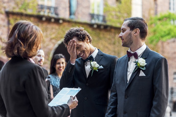 Gay man looking at shy partner while standing in front of priest during wedding ceremony
