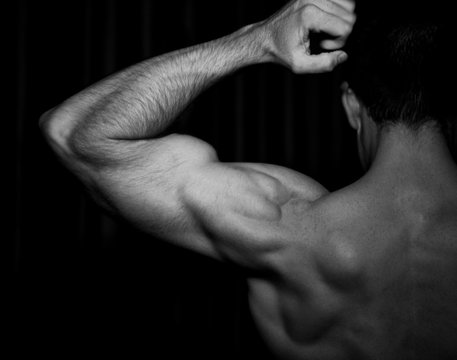 Rear view of bare-chested man flexing bicep muscles