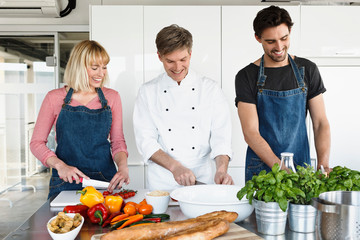 Chef and couple in kitchen slicing vegetables